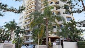 A high-rise hotel with multiple balconies, a central entrance with a staircase, and a parking area with cars. - Voyager Resort (Broadbeach)