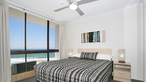 A hotel room with a large bed, a nightstand, a lamp, and a view of the ocean. - Voyager Resort (Broadbeach)