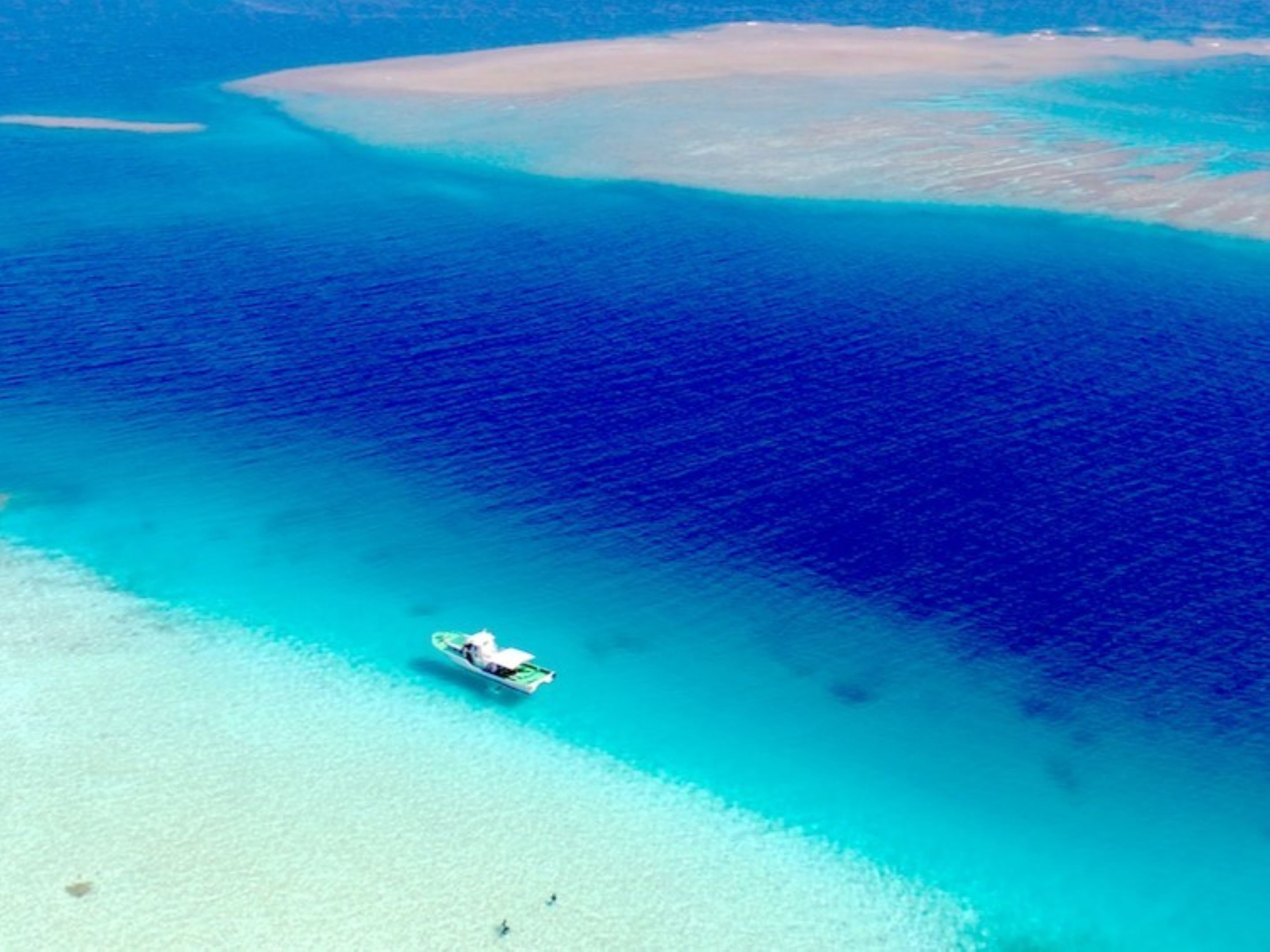 A boat on a turquoise sea with clear waters and a sandy beach.