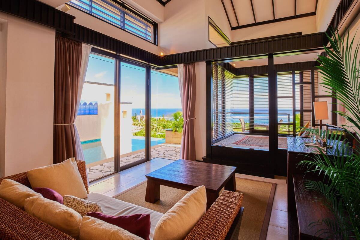 A modern living room with a view of the ocean, a pool, and a dining area with outdoor seating.