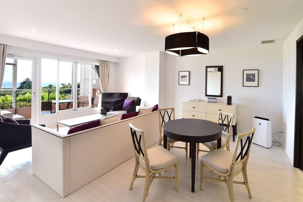 A modern living room with a dining area, large windows, and a view of the outdoors.