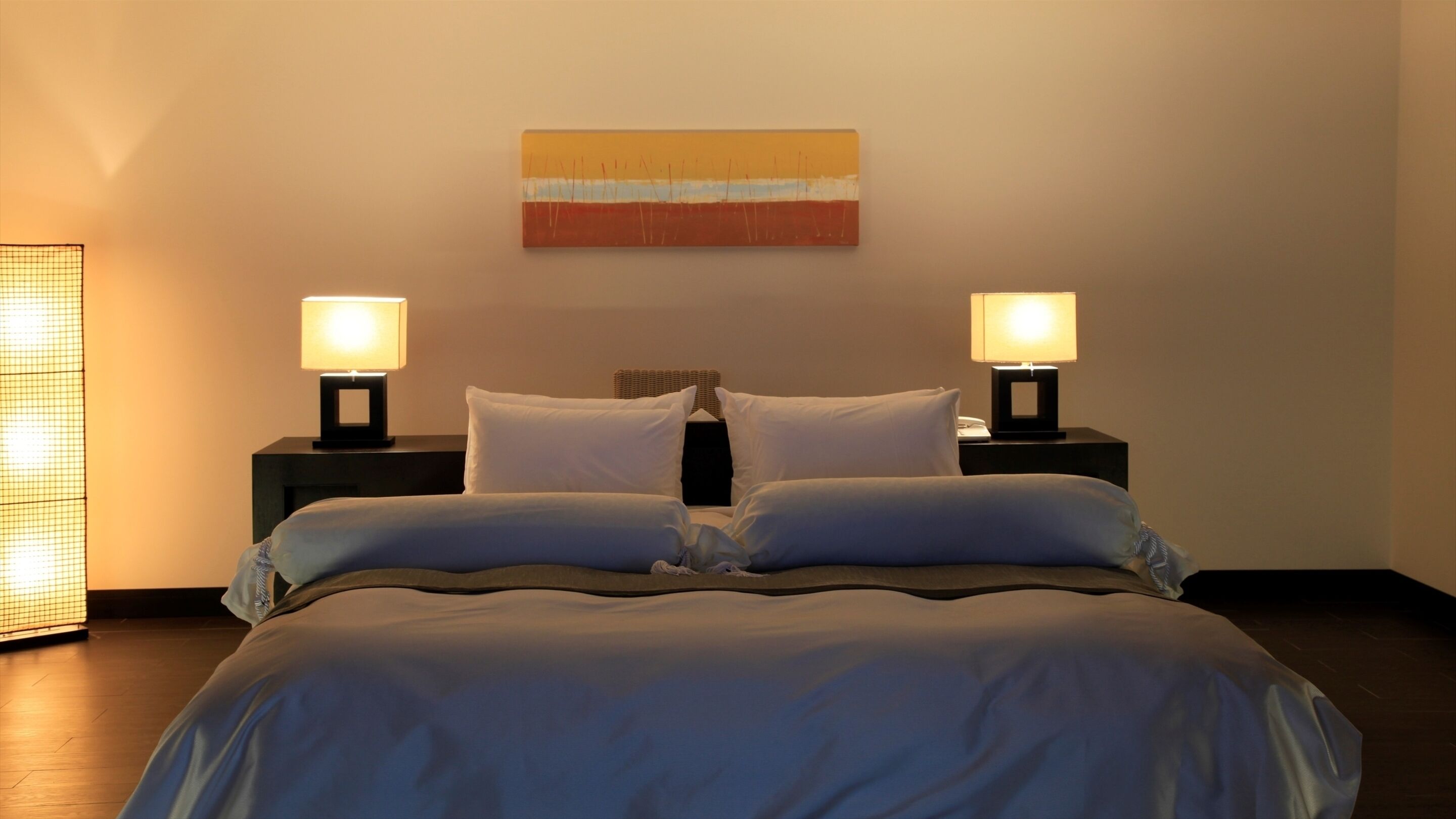 A neatly made bed with white linens, two bedside lamps, and a simple wall art piece above the bed.