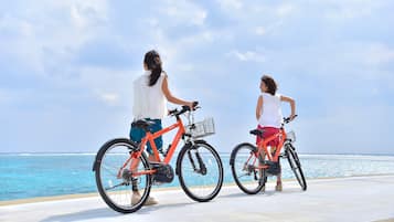 Dos personas en bicicleta junto al mar, con cielo despejado.