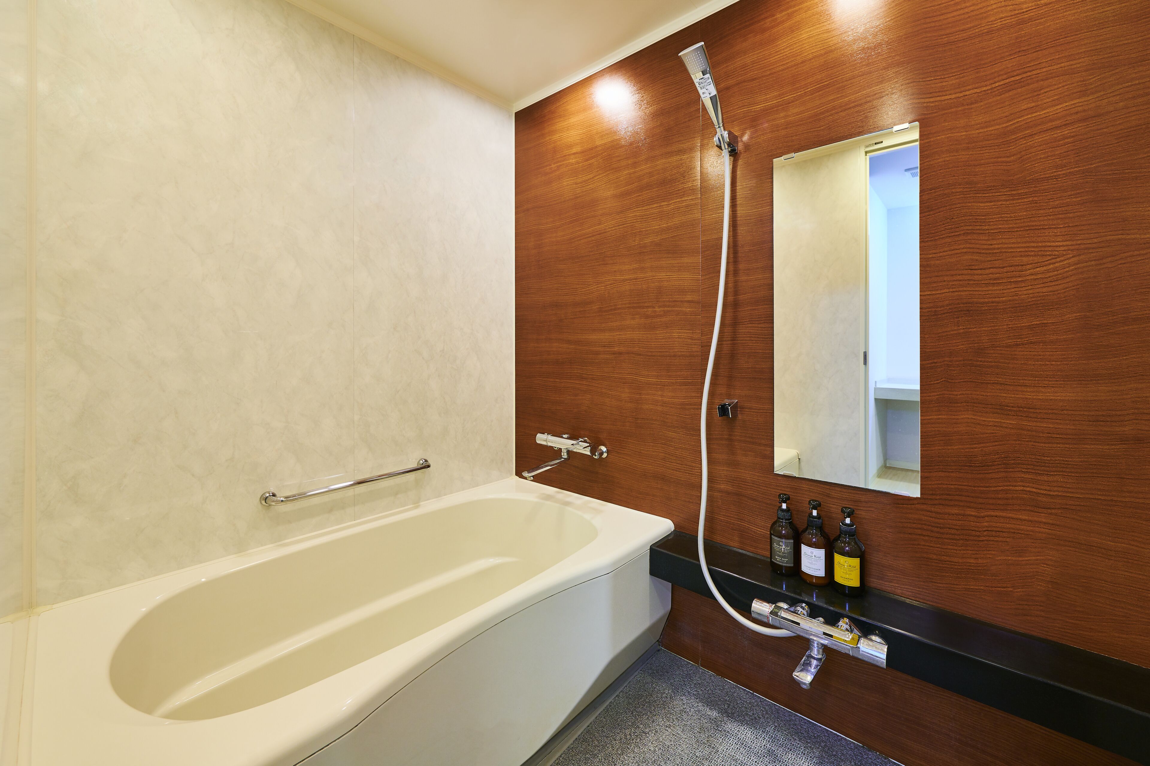 Un baño moderno con bañera, pared de madera, espejo y repisa con artículos de aseo.