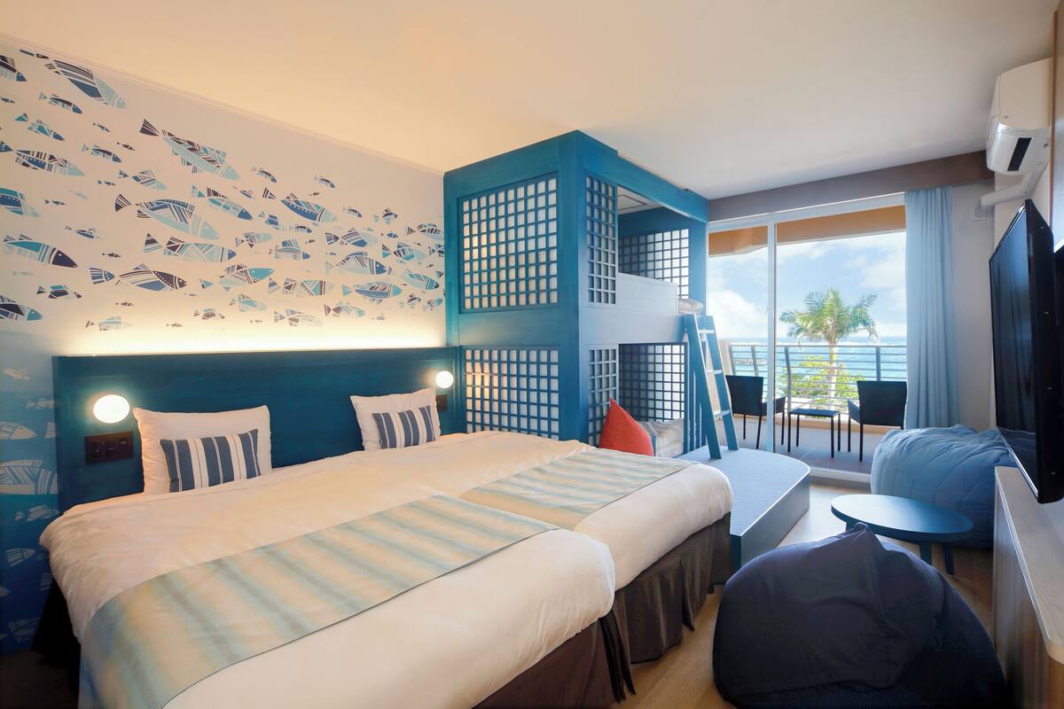 Ein Hotelzimmer mit Bett, Schreibtisch, Stuhl, Fernseher und einem Balkon mit Meerblick.