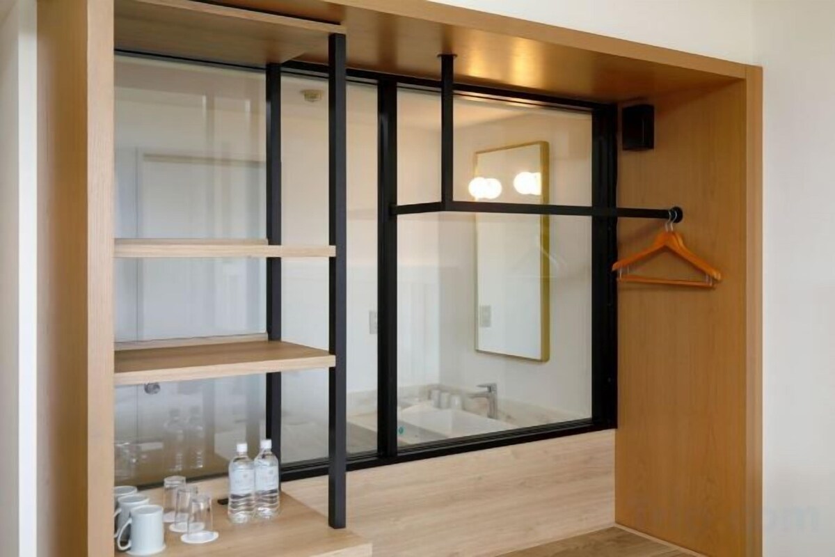 A modern bathroom with a glass partition, wooden shelves, and a mirror with lights.