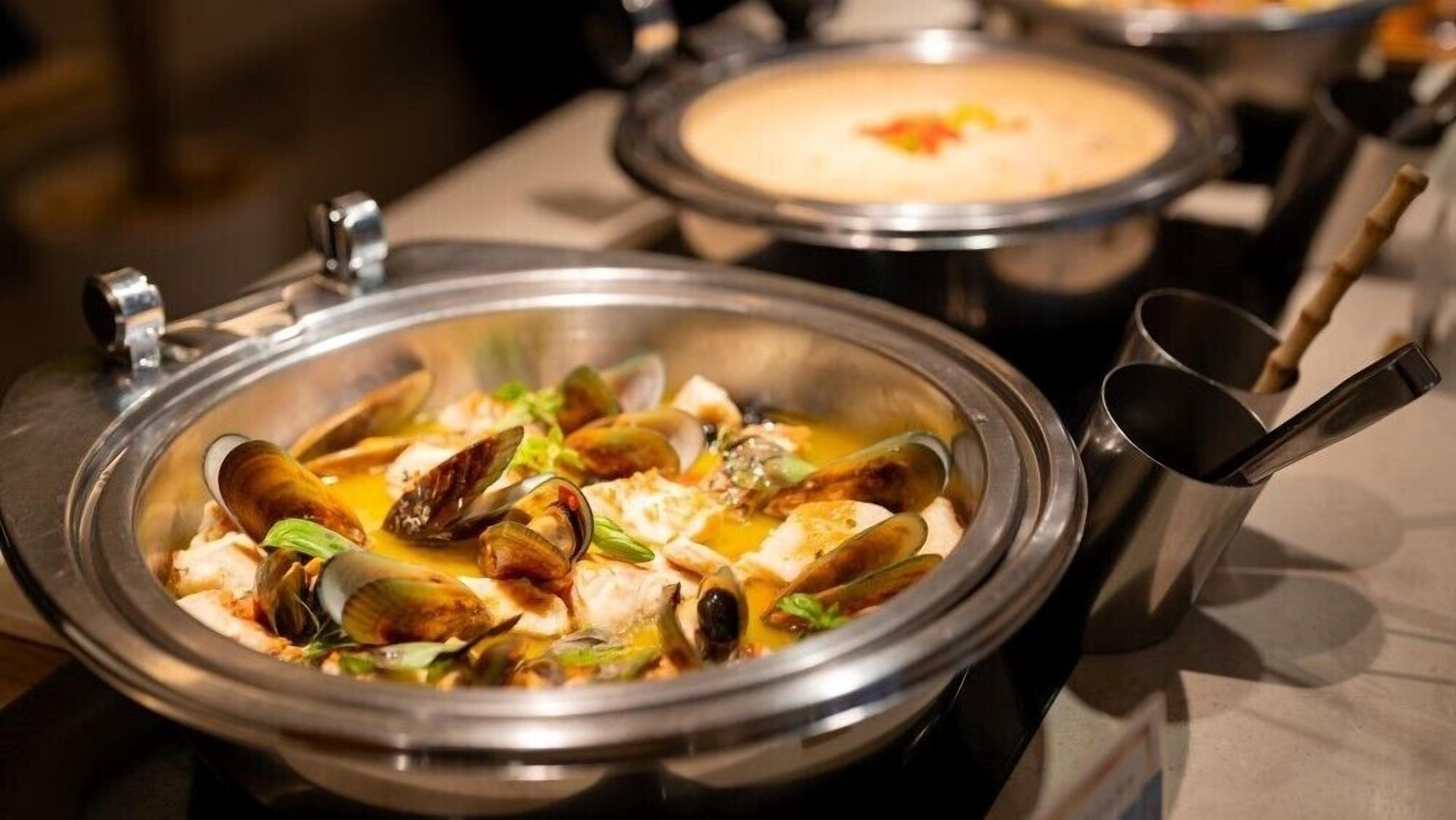 A seafood dish in a bowl with a lid, a ladle, and a spoon nearby.