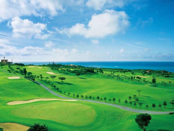 A golf course with a view of the ocean and a distant building.