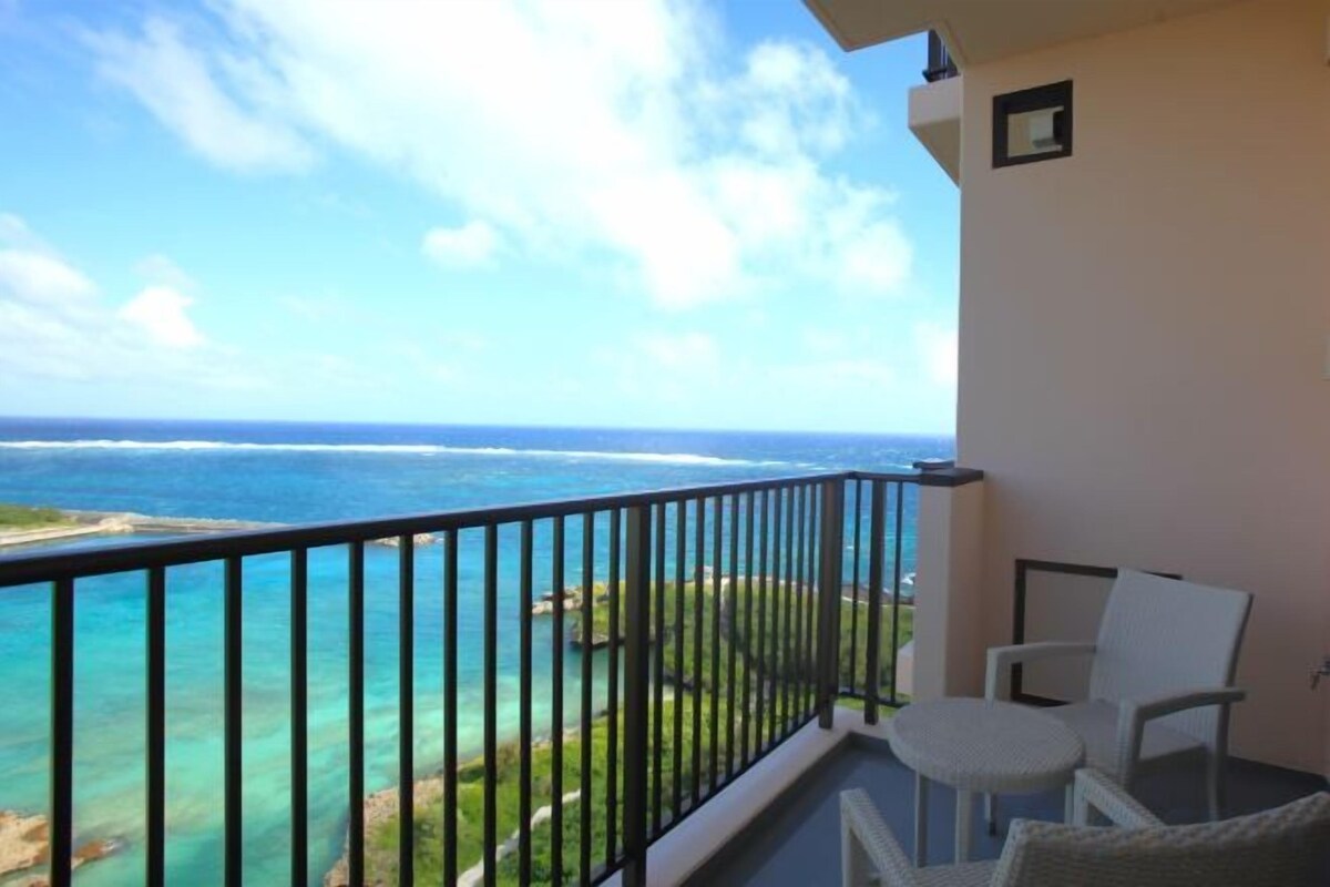 A balcony with a view of the ocean, a chair, and a small table.