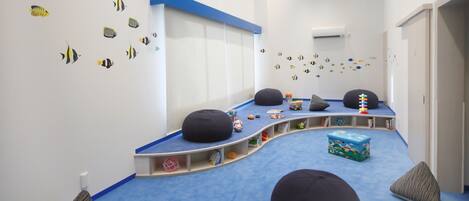 Zona de juegos infantiles con alfombra azul, pufs y adornos en las paredes.