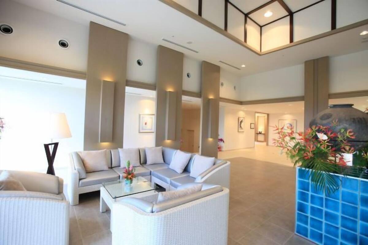 Eine großzügige Lobby mit einer Eckcouch, einem Couchtisch und einem blauen Pflanzgefäß mit Blumen.