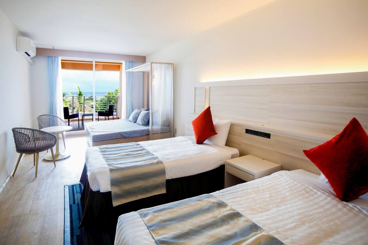 Ein Hotelzimmer mit zwei Betten, einem Balkon mit Blick, einer Sitzecke und einem modernen Design.