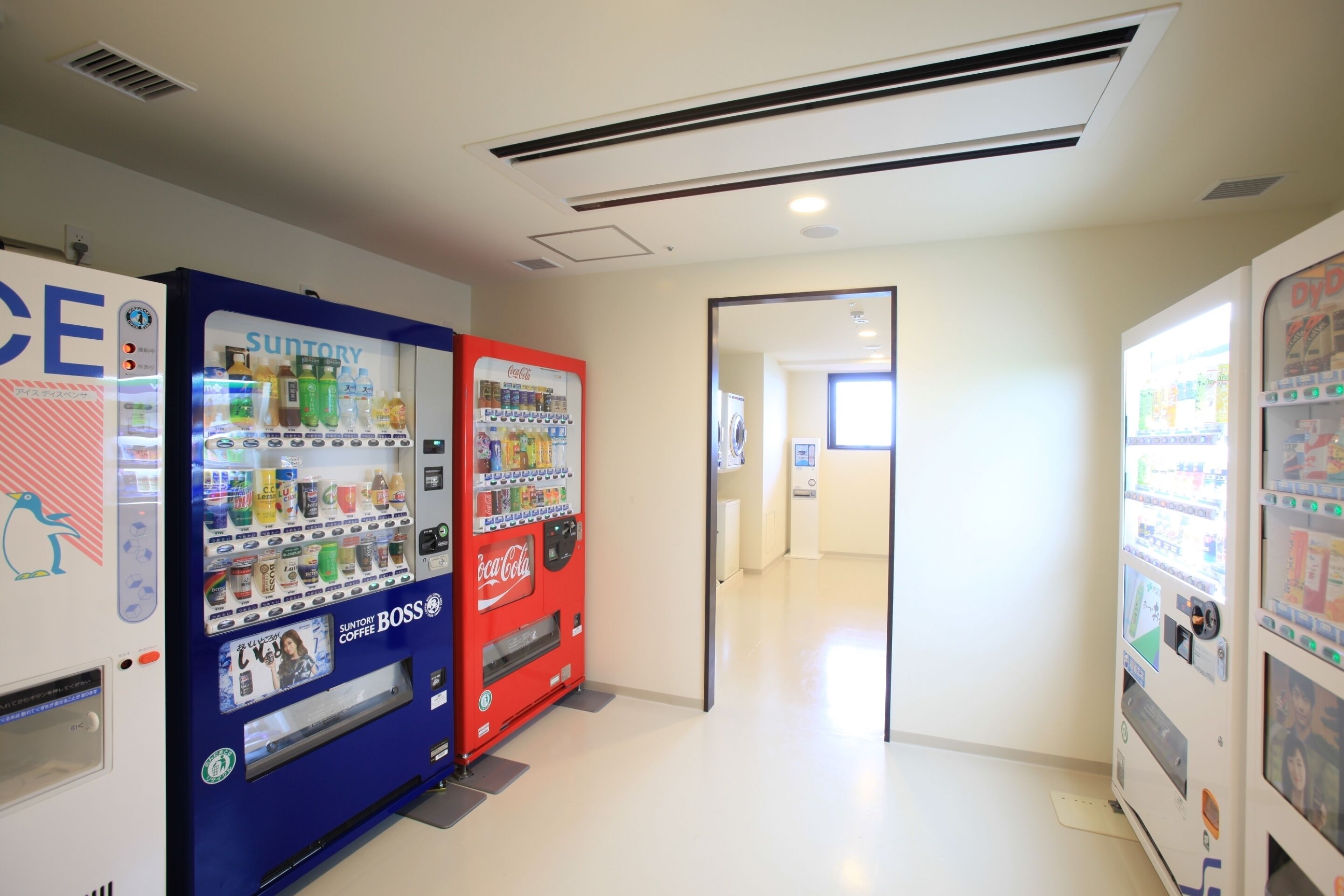 Een gang met automaten, waaronder een Suntory Coffee automaat en een Coca-Cola automaat, en een schone, goed verlichte omgeving.