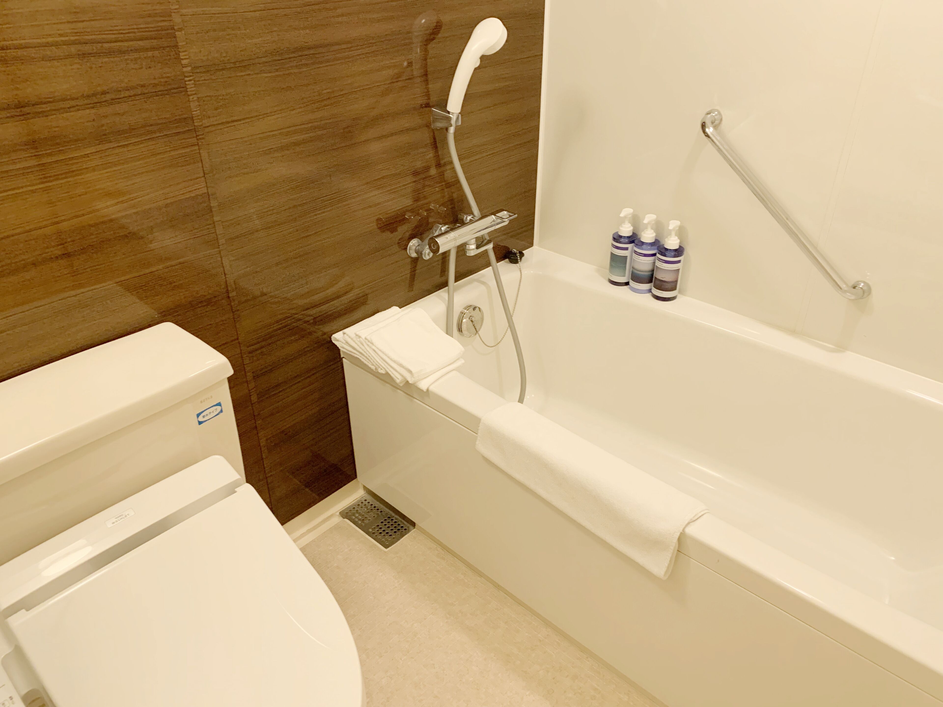 A bathroom with a toilet, a bathtub, and a shower. There are bottles of toiletries on the wall.