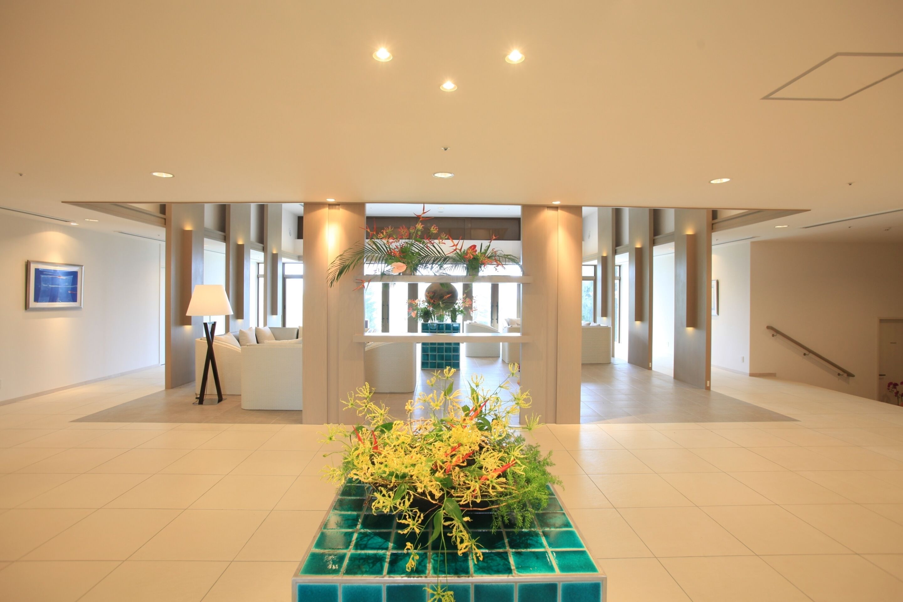 Eine geräumige Lobby mit einer zentralen Blumenkomposition auf einer gefliesten Plattform, einem weißen Sofa und einer Lampe.