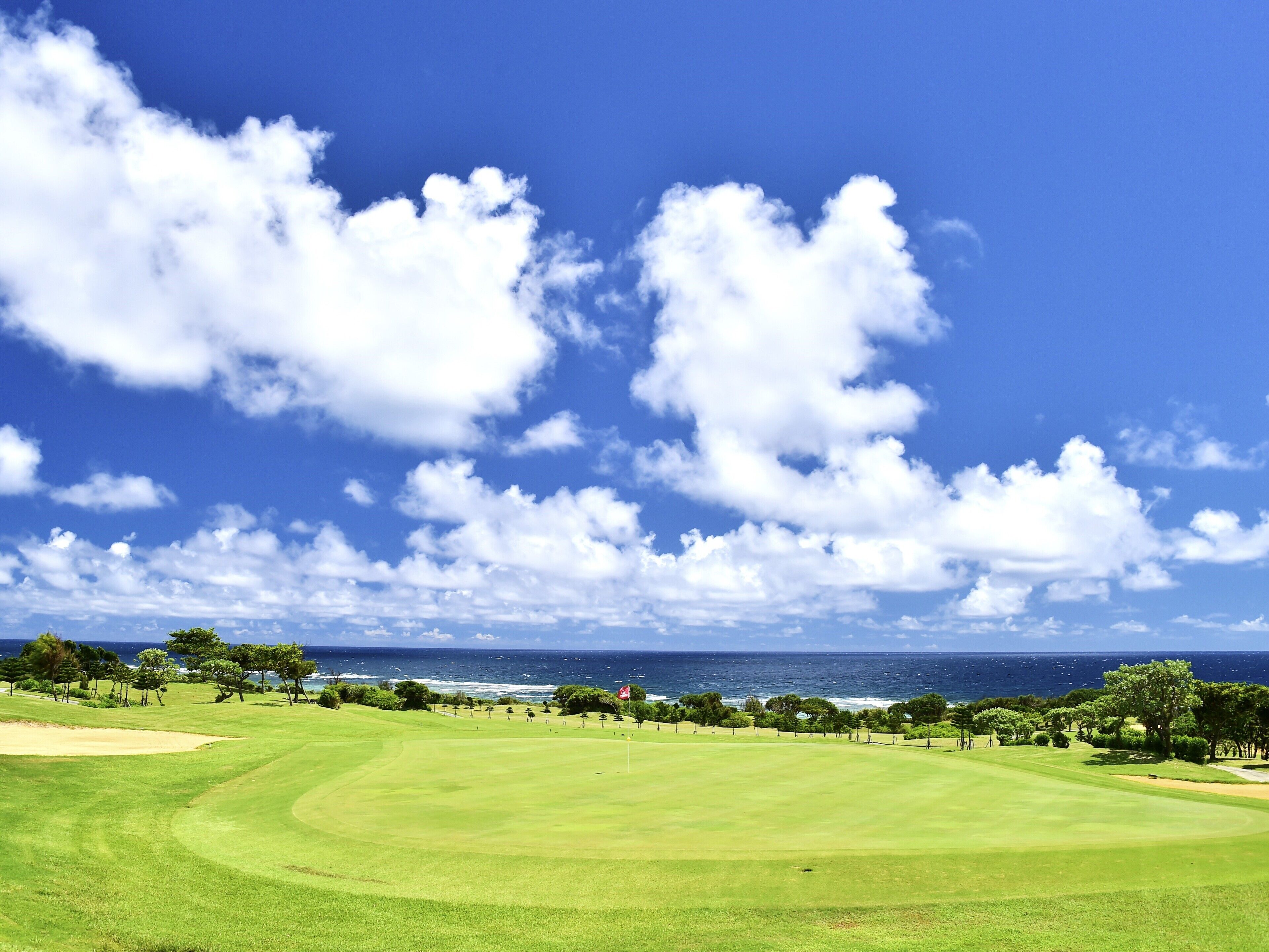 A golf course with a clear view of the ocean and a blue sky with clouds.