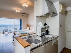 A modern hotel room with a balcony, a kitchenette, and a bed with a view of the sea. - Wellness Villa BRISA (Miyakojima)