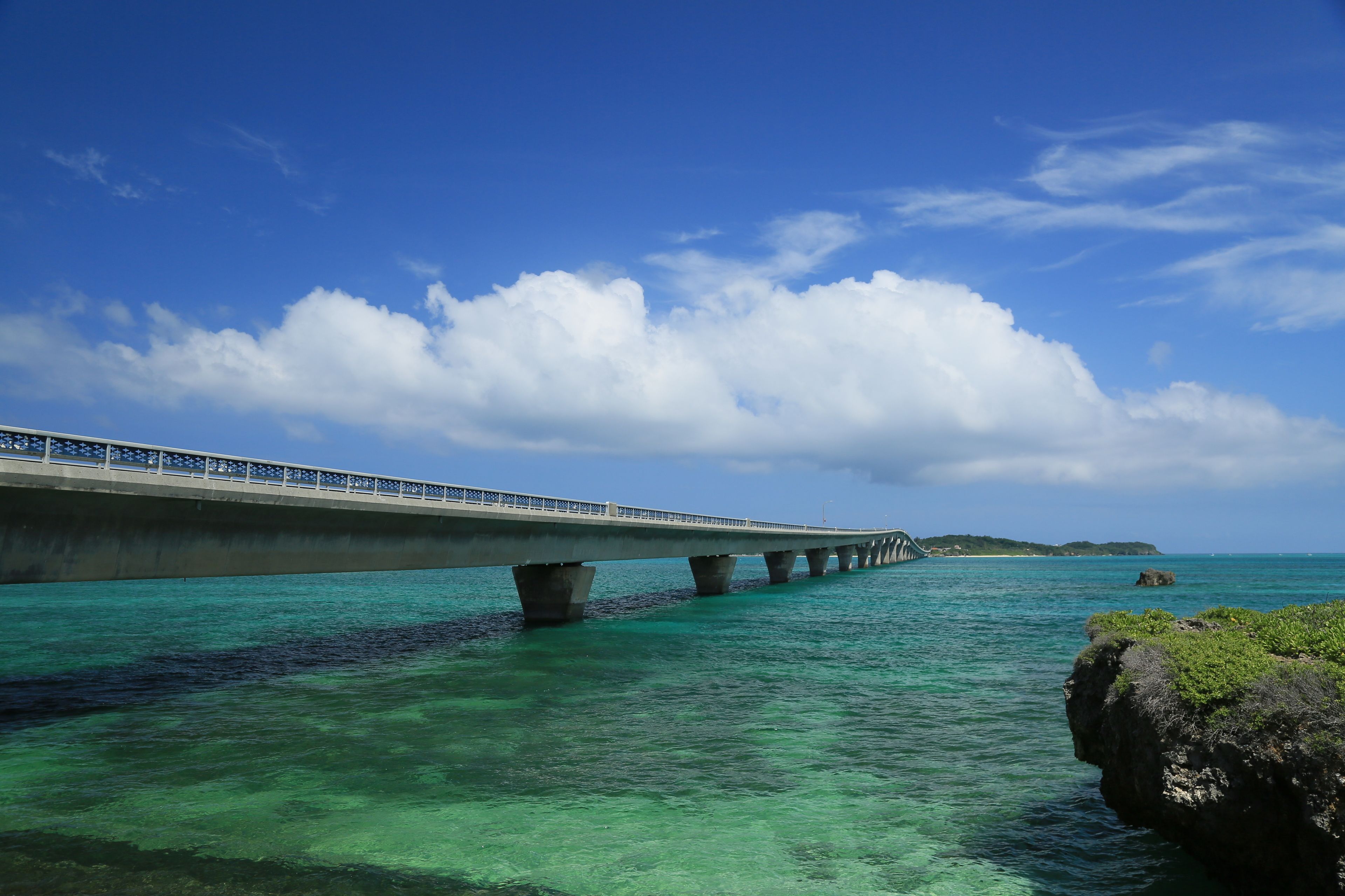 A bridge over clear turquoise water with a rocky outcrop on the right.