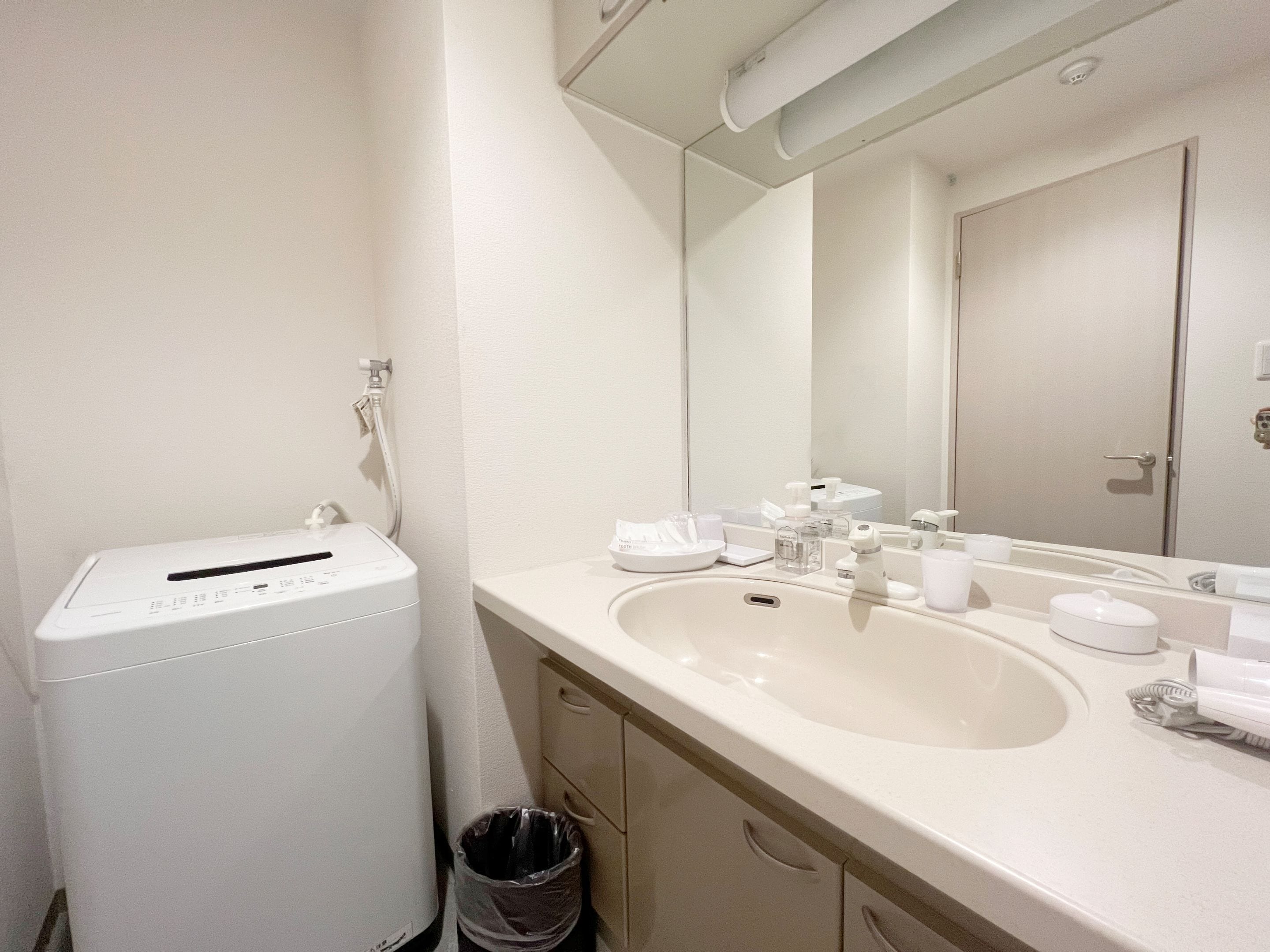 A bathroom with a white sink, mirror, and a white washing machine.