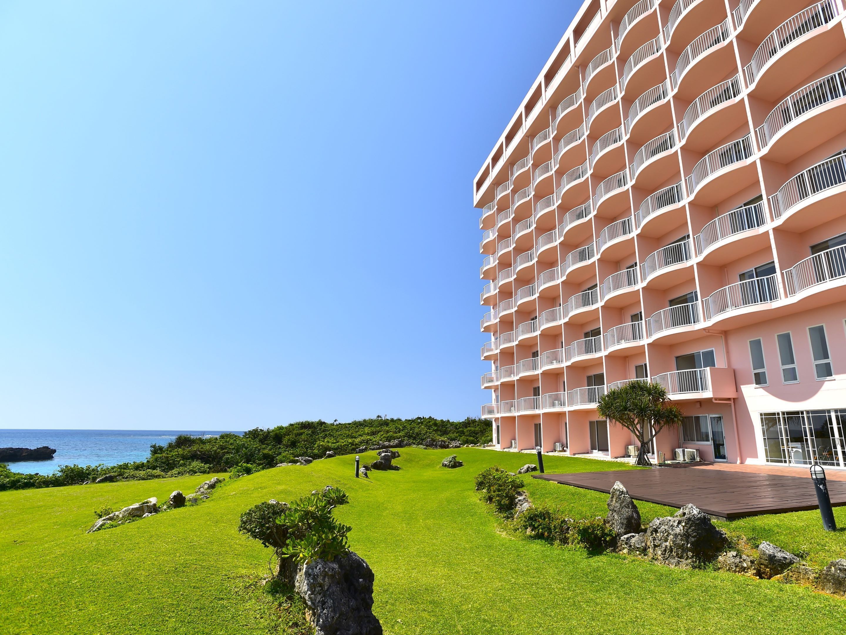 Un hotel de varios pisos con balcones, un césped cuidado y vistas al océano.