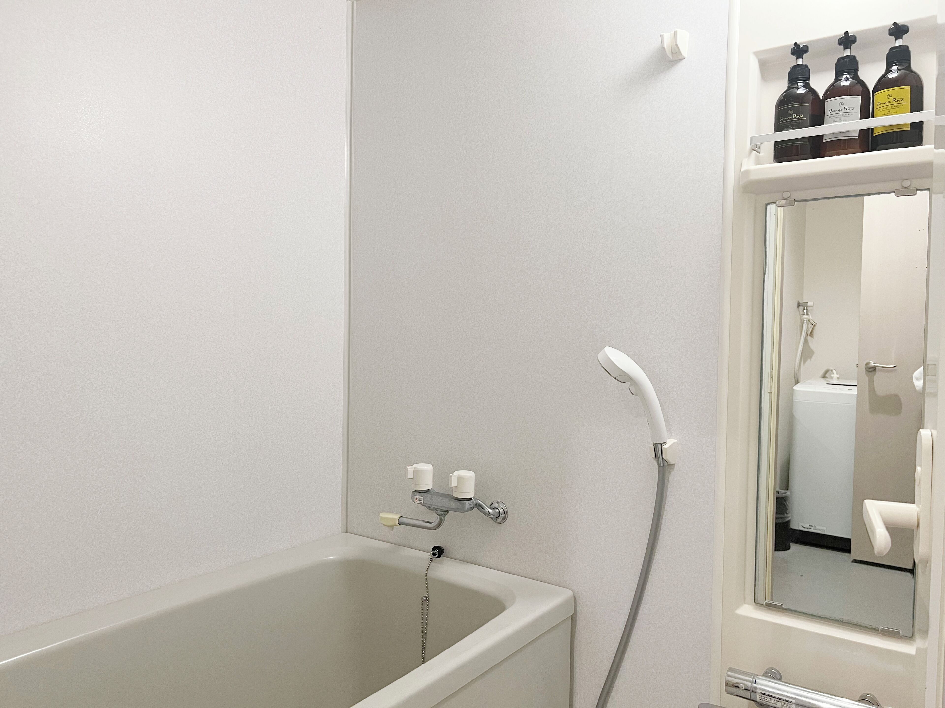 Un bagno con vasca, doccia e uno specchio. Si vedono flaconi di sapone sopra lo specchio.