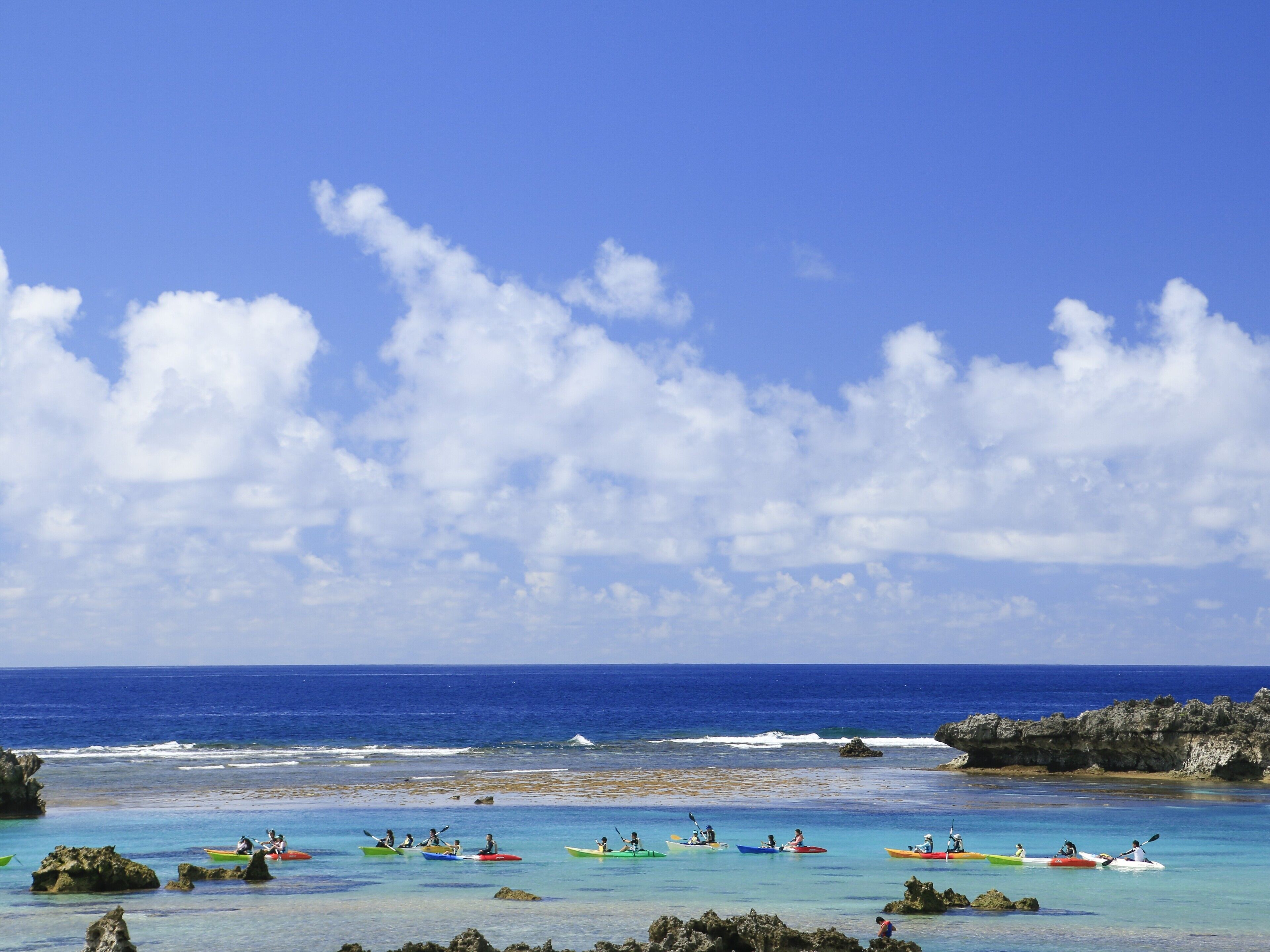 A beach with kayaks lined up near the shore, calm water, and a clear sky.