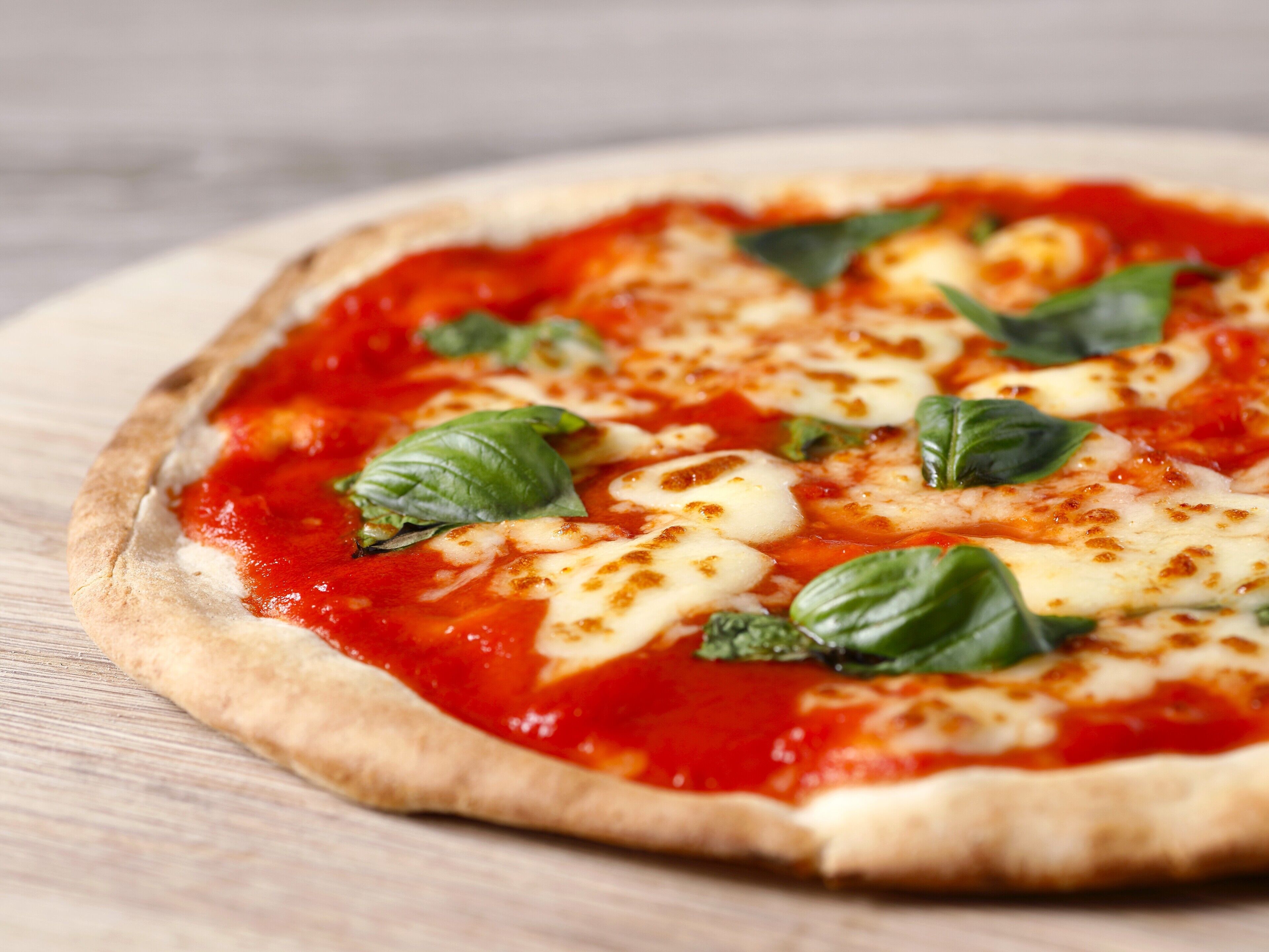 A pizza with tomato sauce, cheese, and basil leaves on a wooden surface.