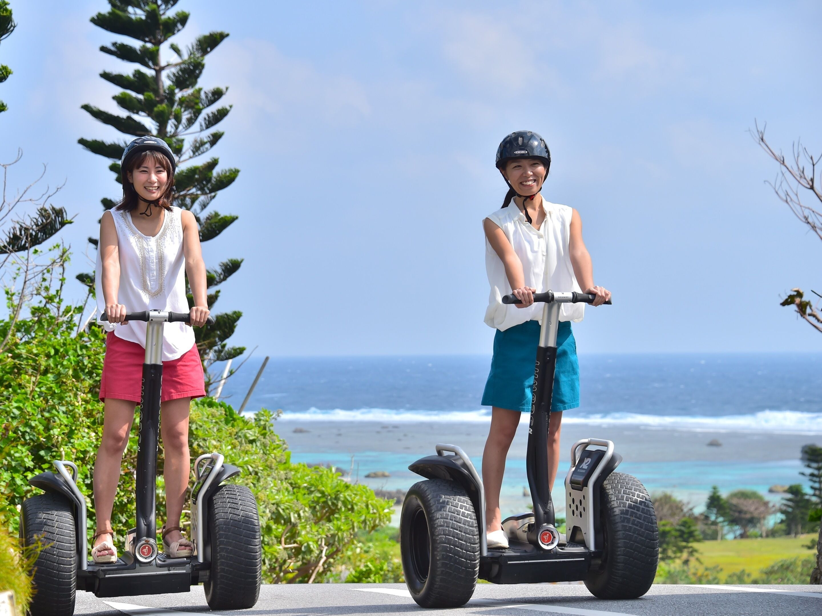 Two people on Segways near a coastal area with trees and ocean views.
