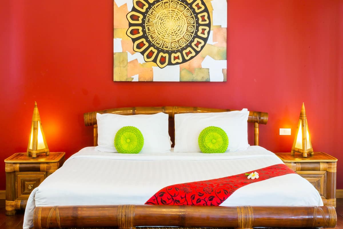 A room with a bed, red walls, a decorative wall piece, and two bedside lamps.