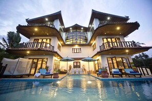 Una casa de dos pisos con piscina, balcones y mobiliario exterior.