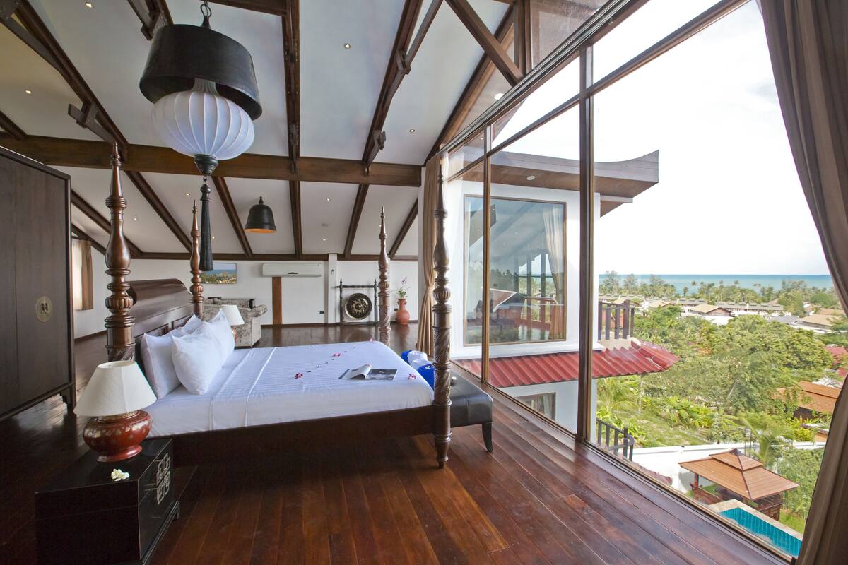 A spacious bedroom with a large bed, wooden beams, a view of the landscape, and a balcony.