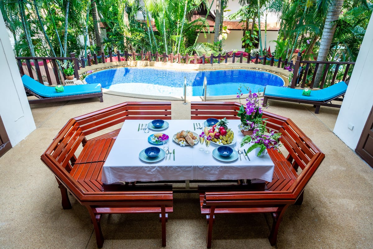 A dining area with a pool view, wooden furniture, and a table set for a meal.