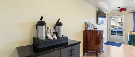 A reception area with a coffee station, a wooden cabinet, and a door leading outside.