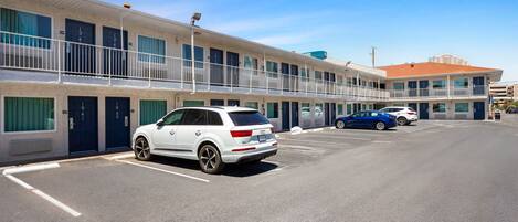 A multi-story motel with a row of rooms on the ground floor, a parking lot, and a clear blue sky.