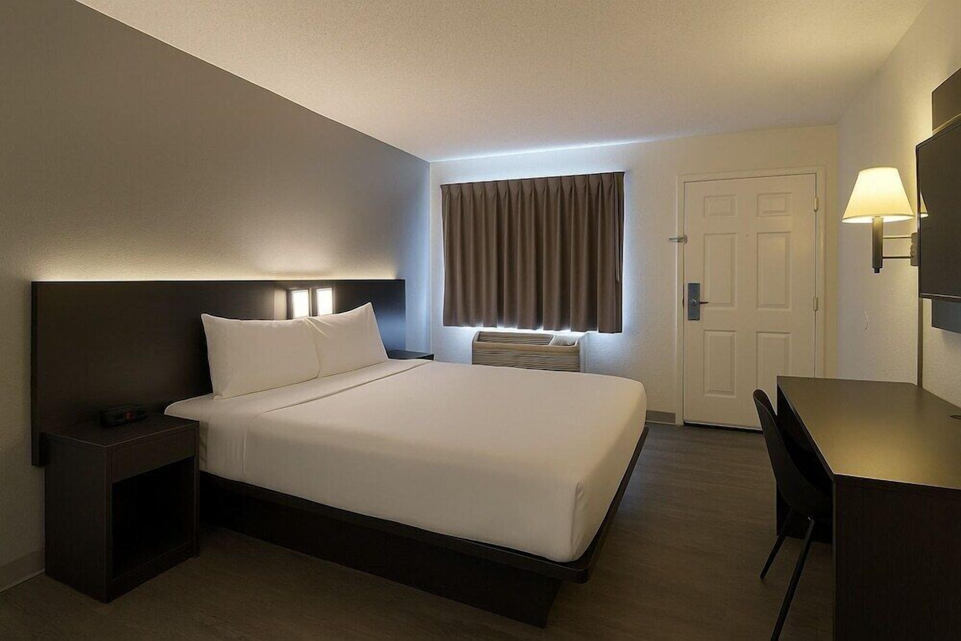 Una habitación de hotel con cama, mesita de noche, lámpara y escritorio con silla.