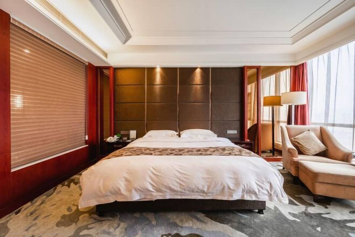 A hotel room with a large bed, a chair, a nightstand, and a lamp.