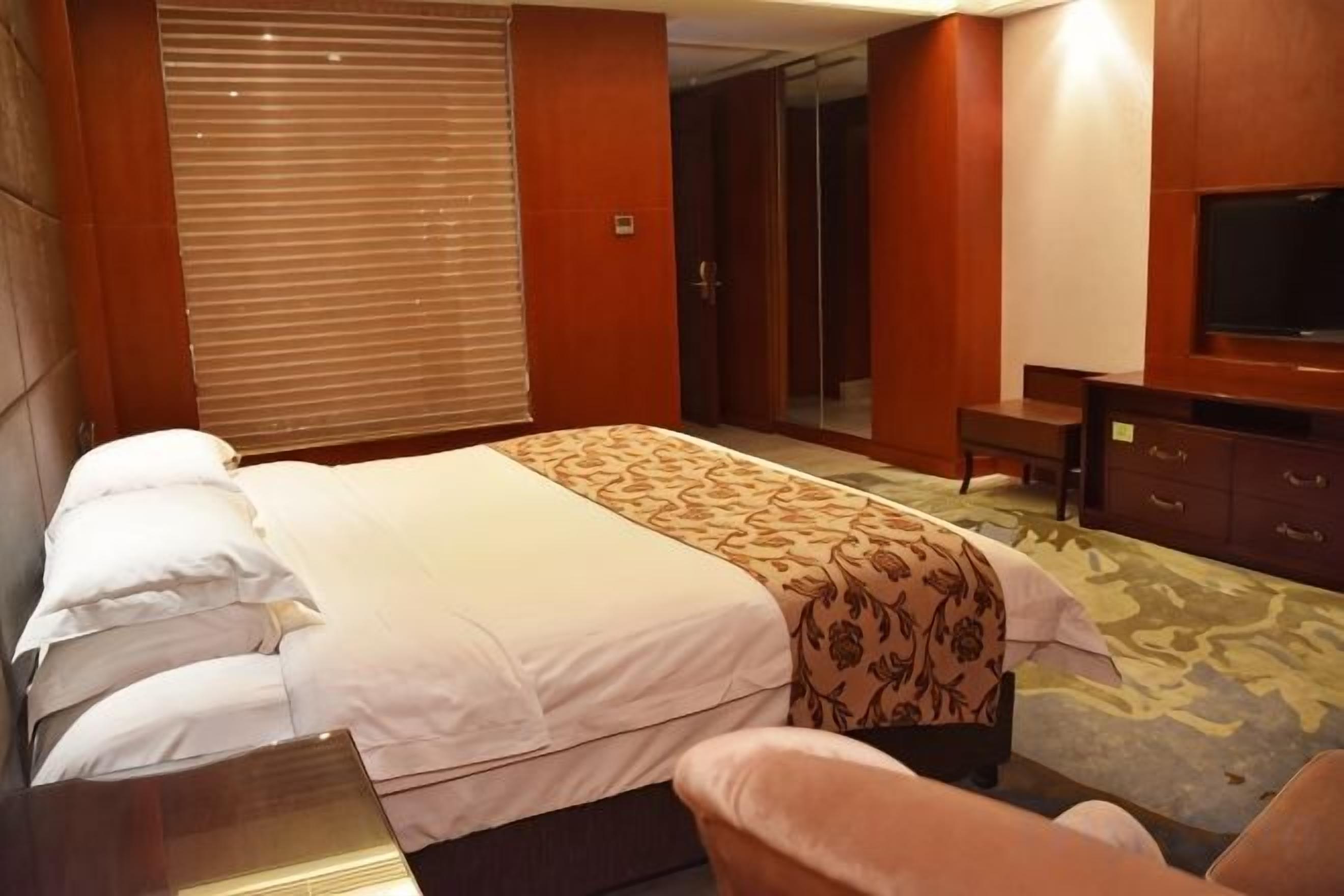 Une chambre d’hôtel comprenant un lit, un bureau, une chaise, une télévision et une armoire.