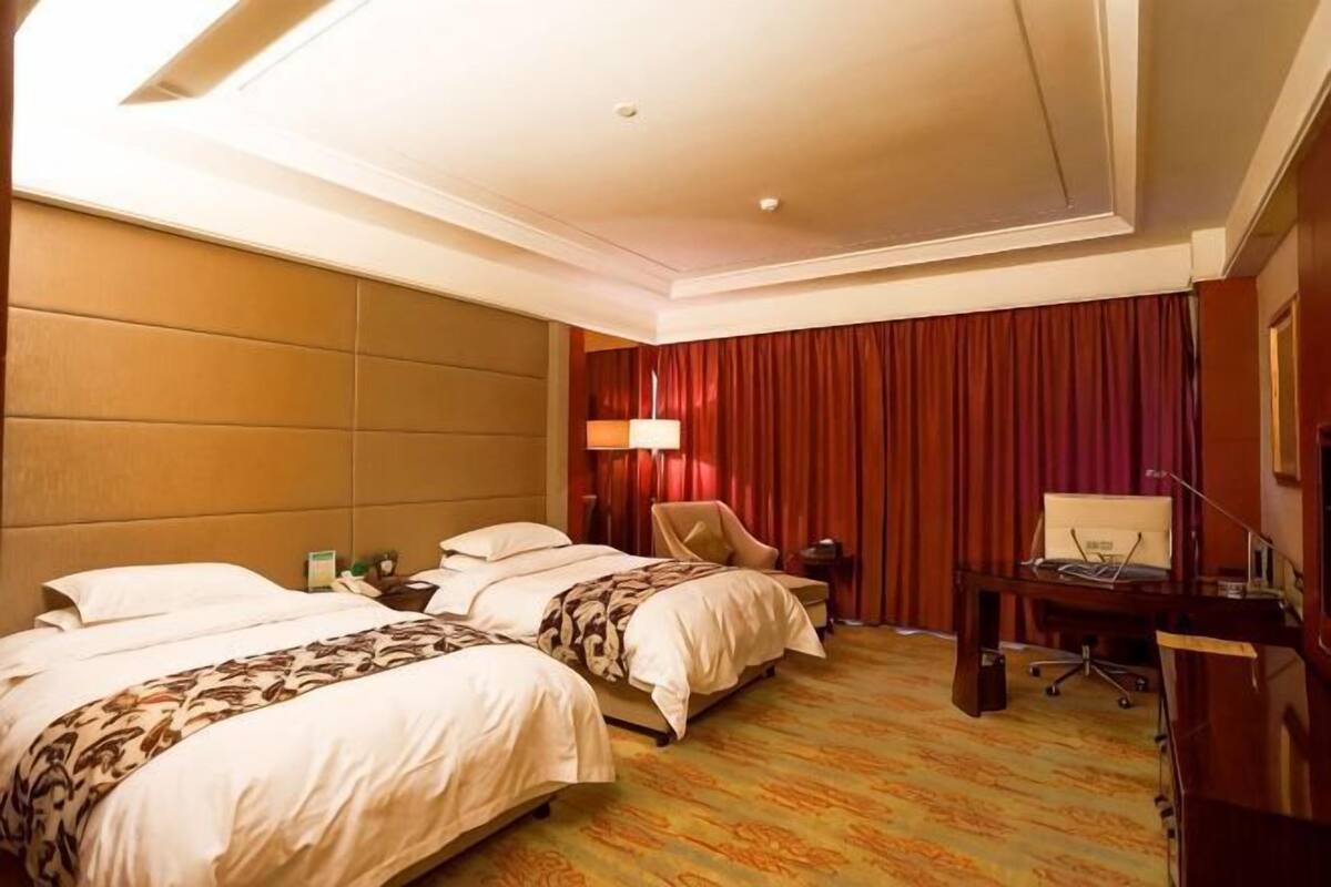 A hotel room with two beds, a desk, a chair, a lamp, and a red curtain.
