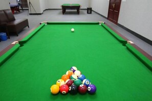 A pool table with a green felt surface and a set of billiard balls arranged in a triangle formation. - Wanfu International Hotel (Xianyang)