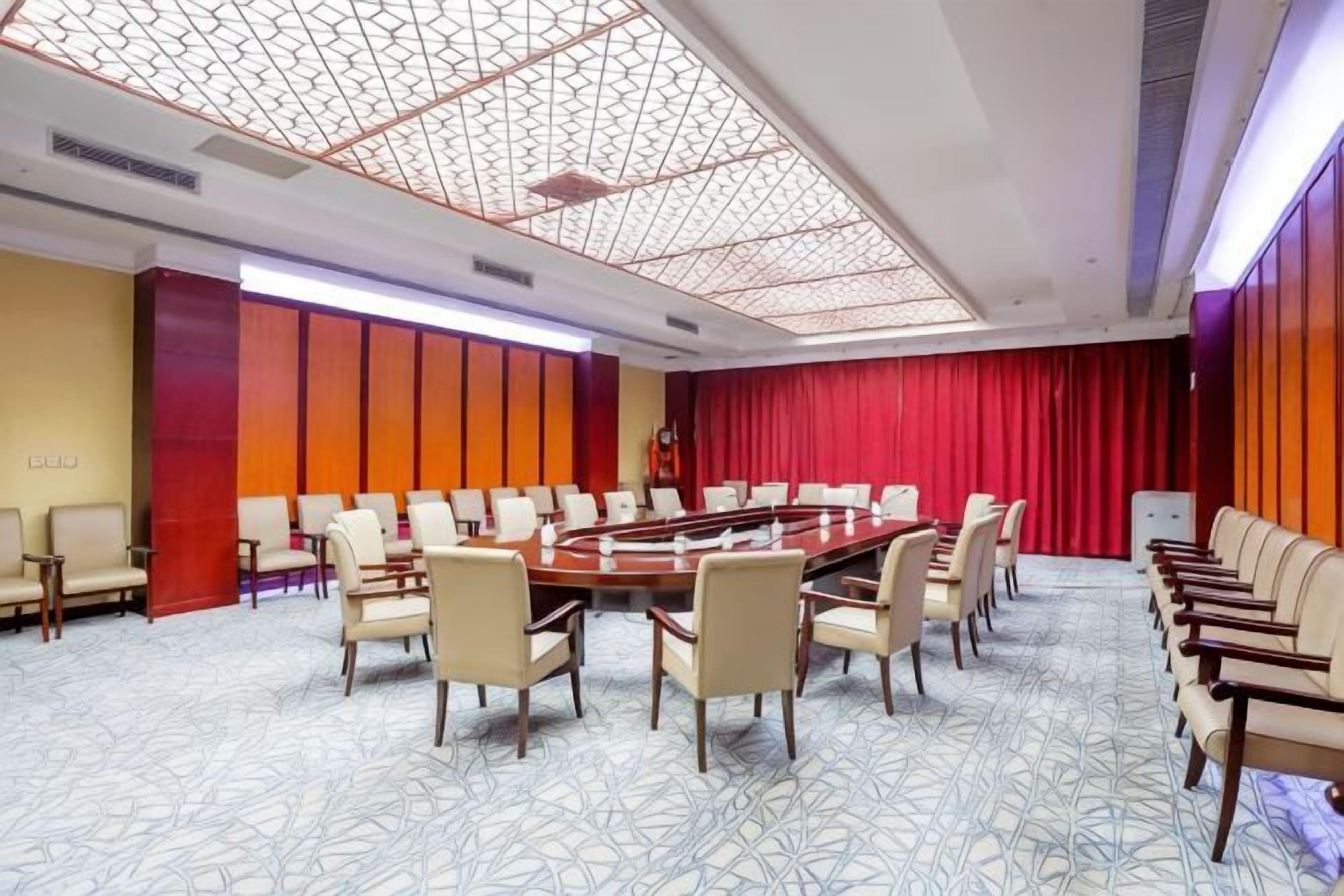 A conference room with a long table, chairs, and a red curtain backdrop.