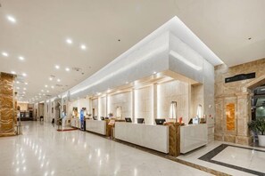 Egy modern szállodai recepció, márványból készült pulttal, digitális bejelentkezőállomással és nagy, jól megvilágított belső térrel.