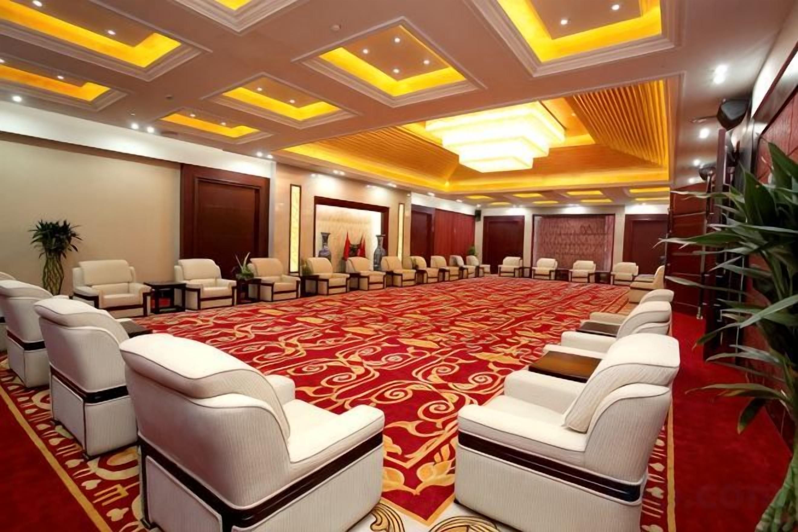 A conference room with a long table and rows of chairs, a red carpet, and a modern ceiling design.