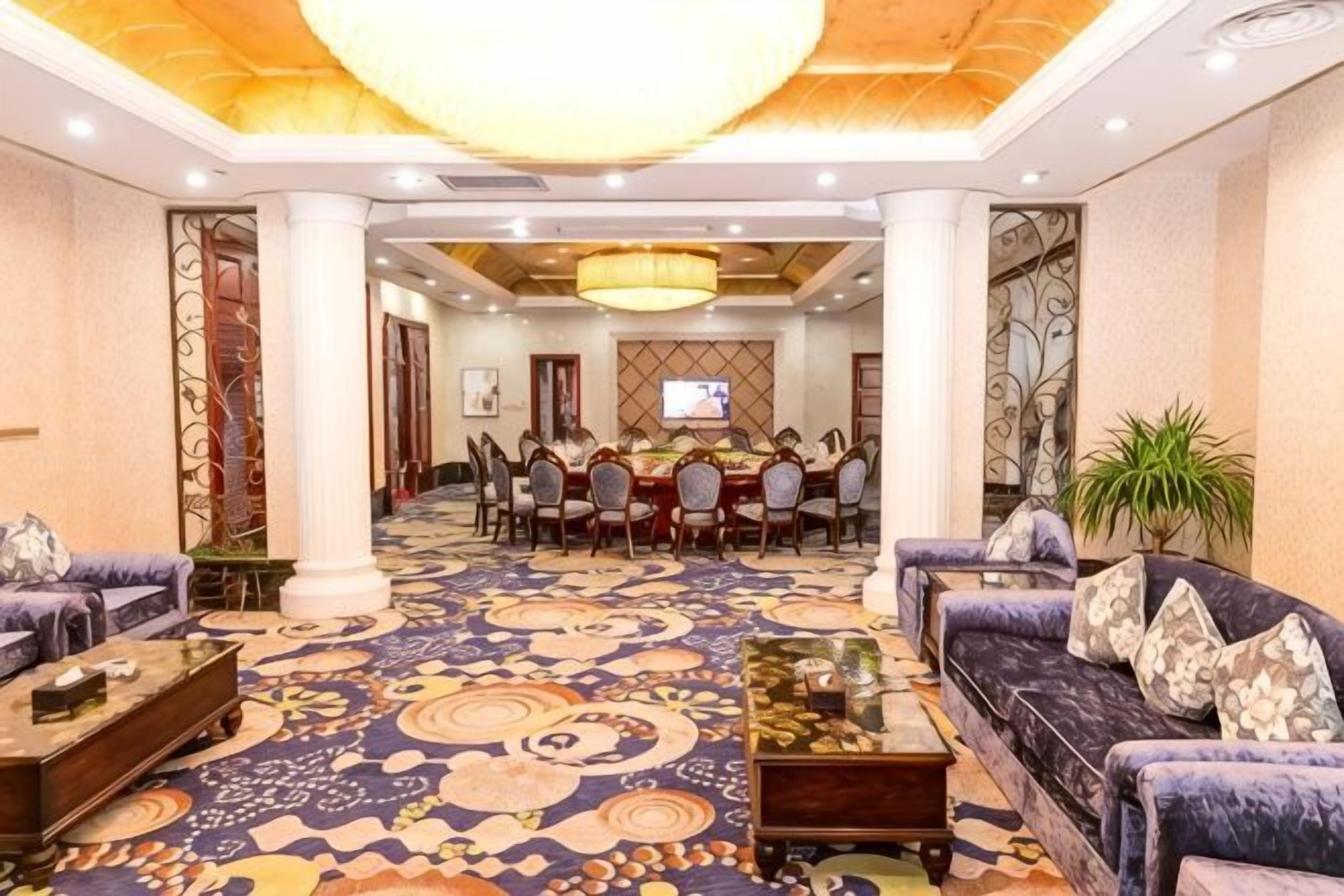 A hotel lobby with a large dining table, sofas, and a carpeted floor.
