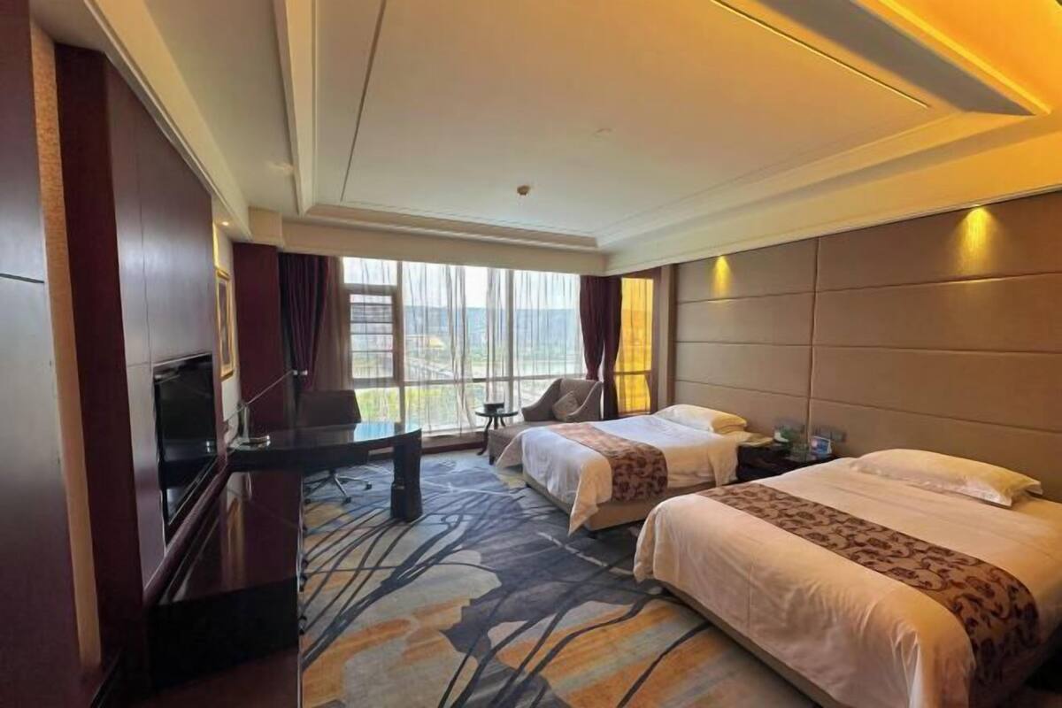 A hotel room with two beds, a desk, a TV, and a view of the outdoors.