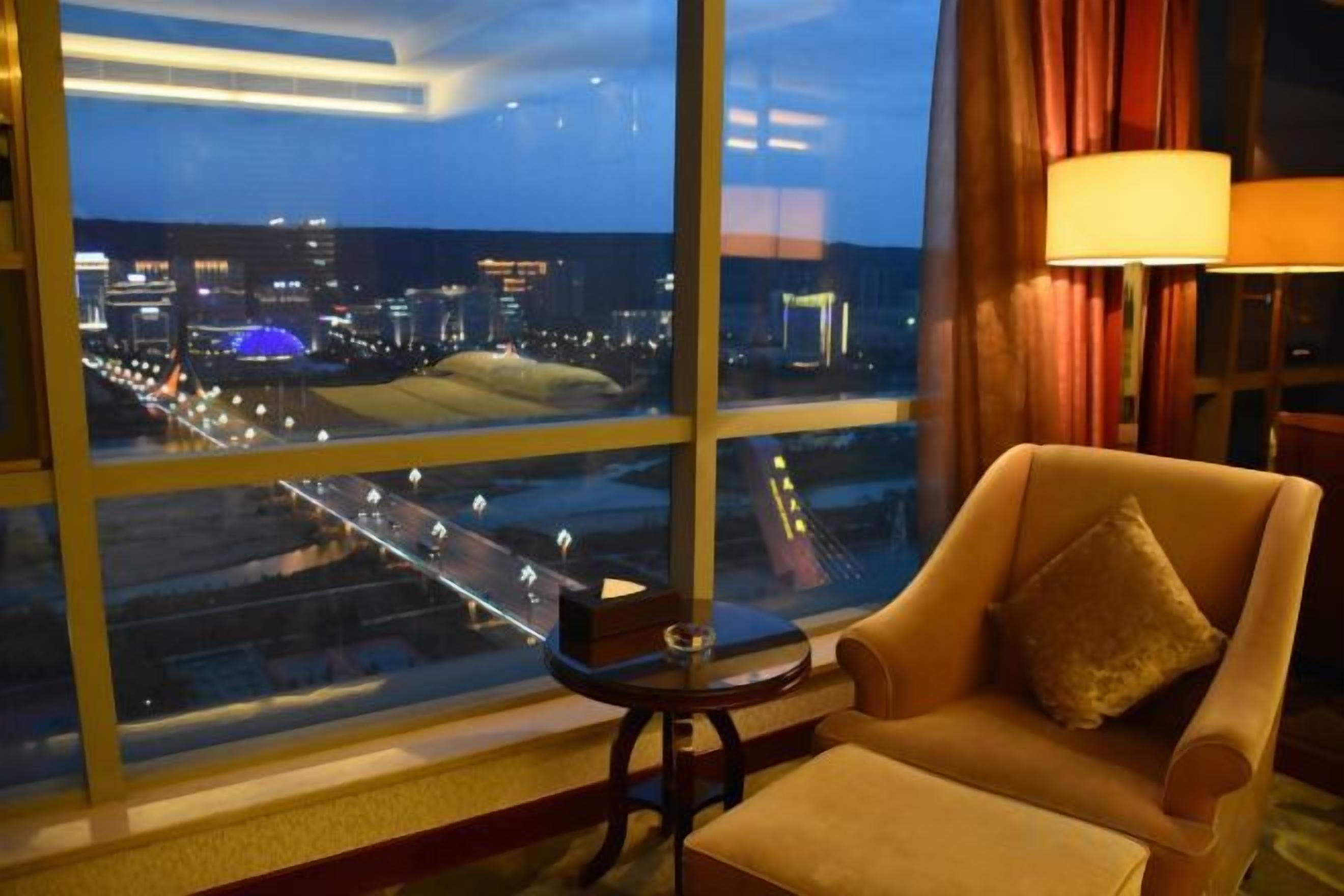 Une chambre d’hôtel avec une grande fenêtre, une chaise, une petite table et une lampe.