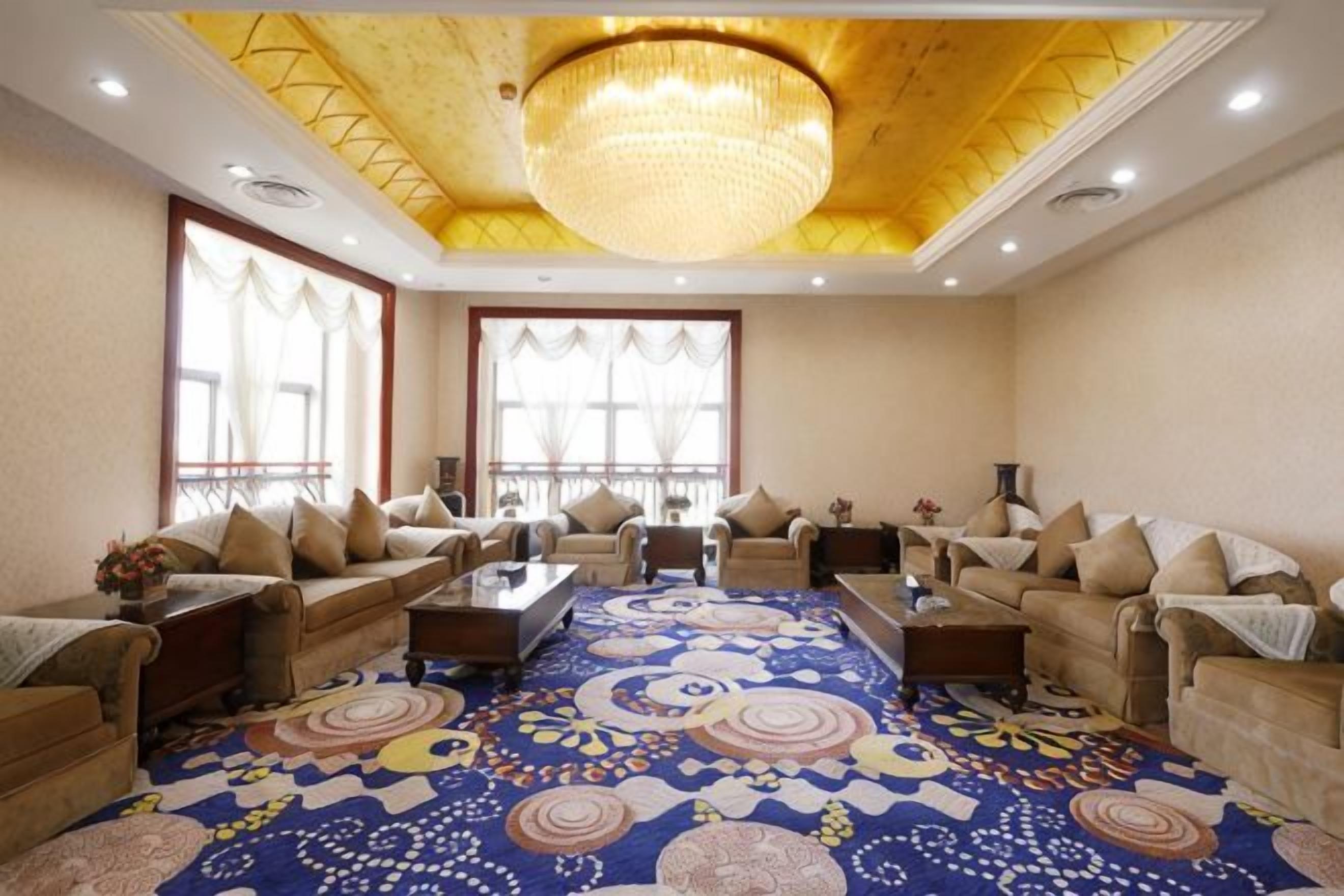 A spacious room with multiple sofas, a patterned carpet, and a large chandelier.