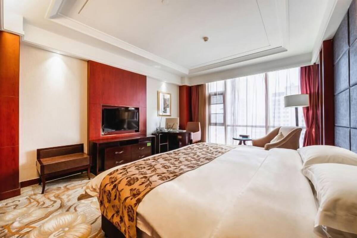 A hotel room with a large bed, a TV, a desk, and a chair.