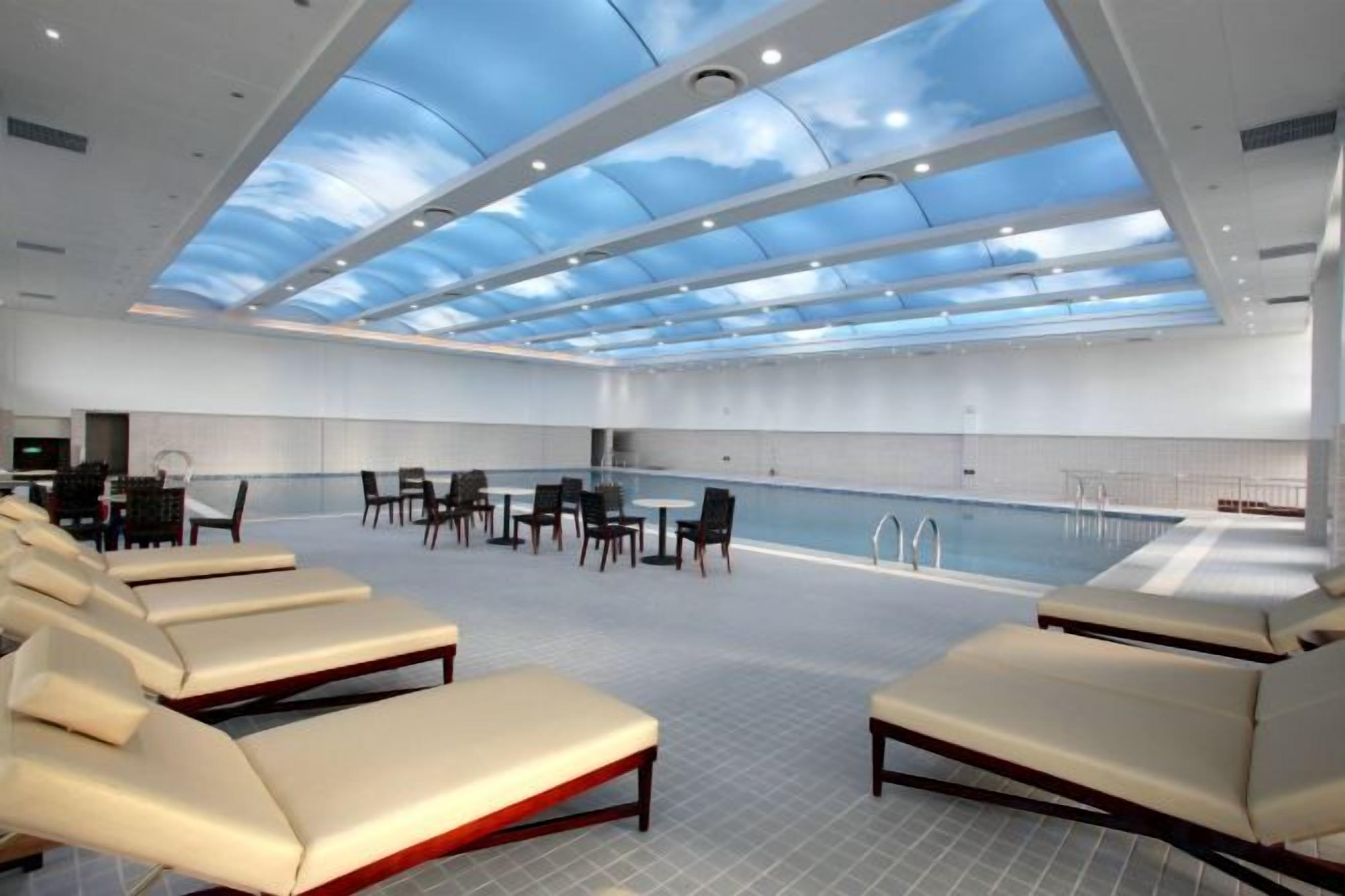 A spacious indoor swimming pool area with lounge chairs and a high ceiling with skylights.