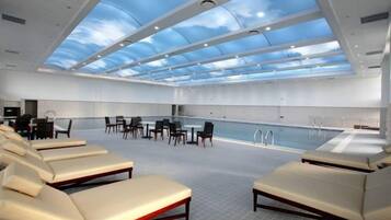 A spacious indoor swimming pool area with lounge chairs and a high ceiling with skylights.