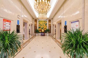 Un hall de hotel con una araña, plantas en macetas y un mural de girasoles.